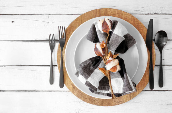 Autumn harvest or thanksgiving dinner table setting with plates, flatware and buffalo plaid napkin. Above view on a white wood background.
