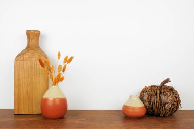 Dekoru ahşap bir rafa, arka planda fotokopi alanı olan beyaz bir duvara doğru düşür. Vazolar, balkabağı ve sonbahar dalları.