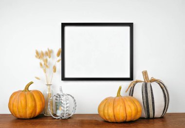 Beyaz bir duvardan sarkan balkabaklarıyla siyah bir çerçeve yap ve ahşap bir rafa düş. Sonbahar konsepti. Boşluğu kopyala.