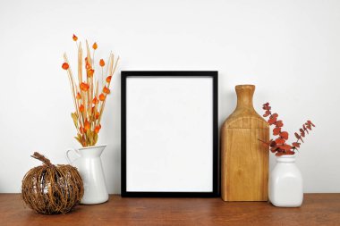 Sonbahar dalları ve ahşap bir rafta dekoru olan siyah bir çerçeve yap. Sonbahar konsepti. Beyaz bir duvara dayalı portre çerçevesi. Boşluğu kopyala.