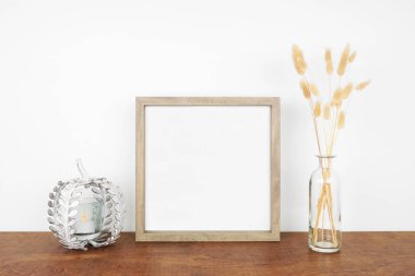 Kare ahşap çerçeveyi sonbahar çimenleri ve beyaz bir duvara karşı ahşap bir rafta balkabağı mumu tutacağı ile süsleyin. Sonbahar konsepti. Boşluğu kopyala.