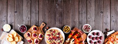 Kış tatili için aperatifler. Koyu ahşap bir arka planda alt sınır görünüyor. Ekmek, şiş, yaban mersinli crostini ve çeşitli parti yemekleri. Boşluğu kopyala.