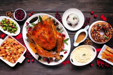 Geleneksel Noel hindisi yemeği. Koyu renk ahşap arka planda en üstteki masa sahnesi. Hindi, patates, sos, meyveli pasta ve erikli puding..