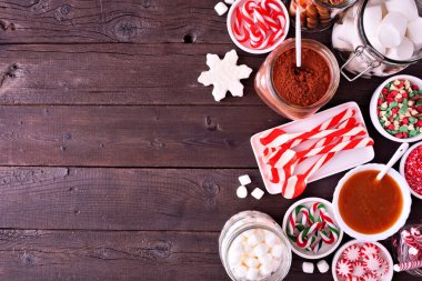 Noel sıcak kakao büfesi, çeşitli tatlı malzemelerle. Koyu bir ahşap arka planda tepeden aşağı görünüm kenarı.