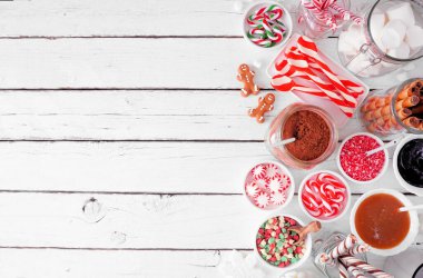 Noel sıcak kakao barı, çeşitli tatlı malzemelerle. Beyaz ahşap arka planda, görüş sınırının üstünde..