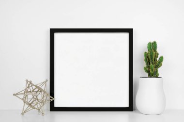 Modern ev dekoru ve bitkiyle siyah kare çerçeve yap. Beyaz bir duvara karşı beyaz bir raf. Geometrik dekorasyon ve kaktüs. Boşluğu kopyala.