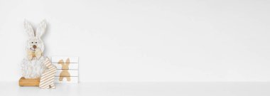 Beyaz bir rafta Paskalya dekoru. Kırsal ahşap tavşanlar ve beyaz bir duvar pankartıyla işaret diliyle. Boşluğu kopyala.