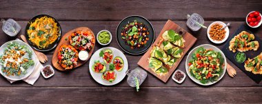 Sağlıklı bitki temelli, düşük karbonhidratlı diyet masası sahnesi. Koyu ahşap arka planda üst manzara. Sebzeli erişte, karnabahar ekmeği ve biftek, lahana salatası, doldurulmuş avokado ve tatlı patates..