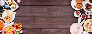 Eğlenceli Paskalya kahvaltısı ya da çifte kahvaltı. Koyu renk ahşap afiş arkaplanda yukarıdan görünüyor. Tavşan gözlemesi, yumurta yuvası, civciv meyvesi ve çeşitli bahar yiyecekleri. Boşluğu kopyala.