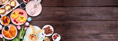 Eğlenceli Paskalya kahvaltısı ya da brunch köşesi sınırı. Koyu ahşap bir arka planda, aşağı manzaranın üstünde. Tavşan gözlemesi, yumurta yuvası, civciv meyvesi ve çeşitli bahar yemekleri. Boşluğu kopyala.