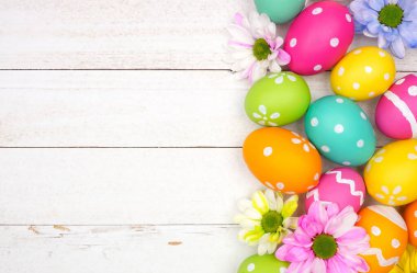 Renkli Paskalya yumurtaları ve bahar çiçekleri. Beyaz ahşap arka planda üst aşağı görüş sınırına karşı. Boşluğu kopyala.