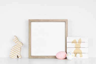 Beyaz bir rafta Paskalya dekoruyla ahşap çerçeve yap. Şık olmayan ahşap tabela, yumurta, tavşan. Beyaz bir duvara karşı kare çerçeve. Boşluğu kopyala.