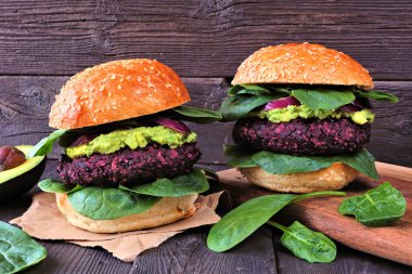 Avokado ve ıspanaklı vejetaryen pancar burgeri. Koyu renk ahşap bir arka plana karşı yan görünüm masası.