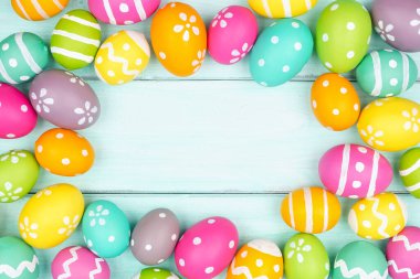 Yumuşak mavi ahşap arka planda renkli Paskalya yumurtası çerçevesi. Boşluğu kopyala.