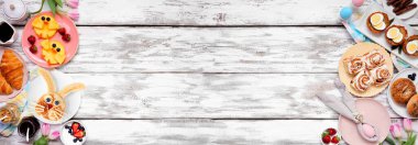 Paskalya kahvaltısı ya da çifte kahvaltı. Beyaz ahşap bir arkaplanda manzaranın üstünde. Tavşan gözlemesi, yumurta yuvası, civciv meyvesi ve bahardaki yiyeceklerden oluşan bir seçim. Boşluğu kopyala.