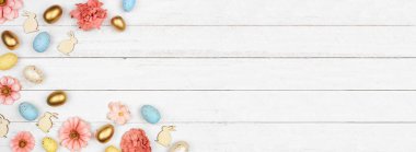 Paskalya sınırında yumurtalar, kağıt çiçekler ve tahta tavşanlar var. Beyaz ahşap bir arka planda yukarıdan aşağıya doğru görünüyor. Boşluğu kopyala.