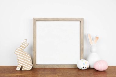 Ahşap çerçeveyi paskalya yumurtası ve beyaz bir duvara karşı ahşap bir rafta tavşan dekoru ile süsleyin. Boşluğu kopyala.