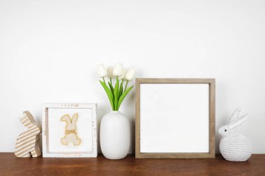 Ahşap bir rafta Paskalya dekoruyla ahşap çerçeve yap. Kırsal tavşanlar, işaret ve lale çiçekleri. Beyaz bir duvara karşı kare çerçeve. Boşluğu kopyala.