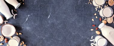 Vejetaryen, bitki bazlı, sütsüz, çift kenarlı. Süt şişelerinde çeşitli tipler ve dağınık malzemelerle dolu bardaklar. Fotokopi alanı olan koyu bir arkaplanda üstten aşağı görünüm.