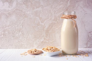 Antika bir şişede yulaf sütü ve malzemeler. Vejetaryen, bitki bazlı, sütsüz. Parlak bir arkaplan karşısında yan görünüm.