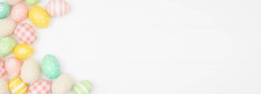 Beyaz ahşap arka planda, çiftlik evi tarzı kumaş ve pastel renkli yumurtalarla Paskalya sınırı. Kopyalama alanı olan üst görünüm.