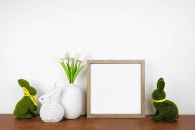Ahşap bir rafta Paskalya dekoruyla ahşap çerçeve yap. Yosun ve örgü tavşanlar ve lale çiçekleri. Beyaz bir duvara karşı kare çerçeve. Boşluğu kopyala.