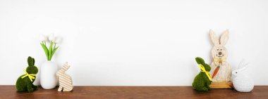 Beyaz bir duvar pankartıyla ahşap bir rafta kırsal tarzda Paskalya dekoru ve bahar çiçekleri. Tavşan süslemeleri ve laleler. Boşluğu kopyala.