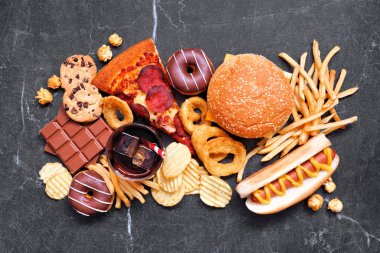 Abur cubur masası sahnesi. Tahsilat karanlık bir zemine saçılmış. Paket servis ve fast food çeşitleri. Pizza, hamburger, patates kızartması, cips, sosisli sandviç, şeker. Görünümün üstünde.