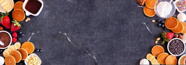 Kahvaltı ya da brunch, açık büfe, çifte büfe. Koyu taştan arka planda yukarıdan aşağıya doğru bir manzara. Çeşitli malzemelerle mini krepler..