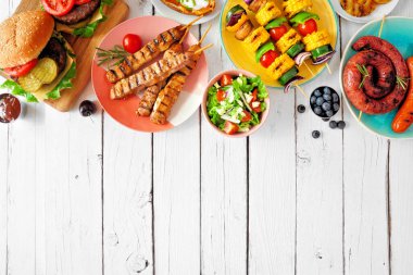 Yaz barbeküsü ya da piknik yemekleri. Çeşitli hamburgerler, ızgara et, sebze, meyve, salata ve patates. Beyaz ahşap arka planda yukarıdan görüntü. Boşluğu kopyala.