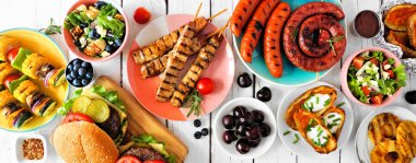 Yaz barbeküsü ya da piknik masası sahnesi. Hamburger, ızgara et, sebze, meyve, salata ve patates. Beyaz ahşap bir arkaplanda tepeden aşağı görünüm.
