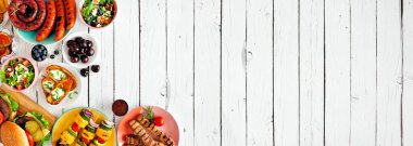 Yaz BBQ 'su ya da piknik yemekleri köşesi sınırı. Çeşitli hamburgerler, ızgara et, sebze, meyve, salata ve patates. Beyaz ahşap arka planda üst manzara. Boşluğu kopyala.