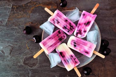 Bir tabak sağlıklı vişneli yoğurt. Masanın üstünde koyu renkli bir arkaplan var..