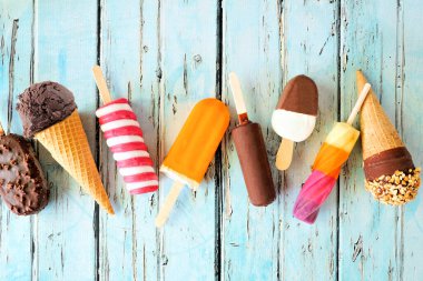 Çeşitli çikolatalar, renkli yaz buzlu dondurmaları ve dondurmalar. Üst görünüm kırsal mavi arkaplana saçılmış.