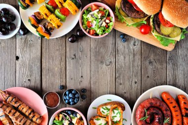 Yaz barbeküsü ya da piknik yemekleri çifte sınır. Çeşitli hamburgerler, ızgara et, sebze, meyve, salata ve patates. Koyu renk ahşap arka planda üst manzara. Boşluğu kopyala.