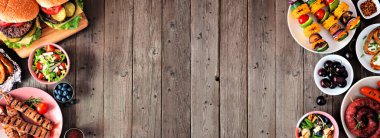 Yaz barbeküsü ya da piknik yemekleri çifte sınır. Hamburger çeşitleri, ızgara et, sebze, meyve, salata ve patates. Koyu renk ahşap afiş arkaplanda yukarıdan görünüyor. Boşluğu kopyala.