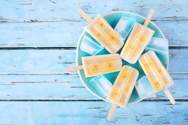 Healthy banana yogurt ice pops. Top down view over a rustic blue background.