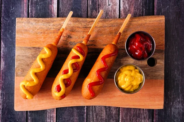 Corn Dogs Different Toppings Wooden Platter Overhead View Dark Wood — Foto Stock