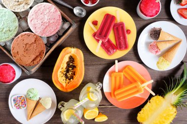 Soğuk yaz yemekleri masası sahnesi. Dondurma, buzlu şeker ve meyve çeşitleri. Koyu bir ahşap arka planda manzaranın üstünde.