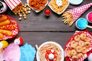 Karnaval temalı yemek çerçevesi koyu bir ahşap arka planda. Kopyalama alanı olan üst görünüm. Yaz festivali konsepti. Sosisli sandviç, huni keki, pamuk şeker ve atıştırmalıklar..