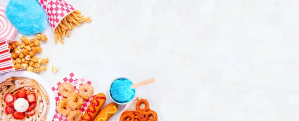 Carnival theme food corner double on a white marble background. Overhead view with copy space. Summer fair concept. Corn dogs, funnel cake and snacks.