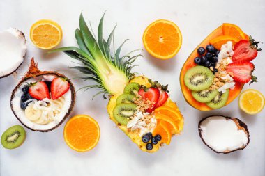 Ananas, papaya ve hindistan cevizli sağlıklı meyveli yoğurt kaseleri. Beyaz mermer zemin üzerinde en üstteki görünüm tablo sahnesi.