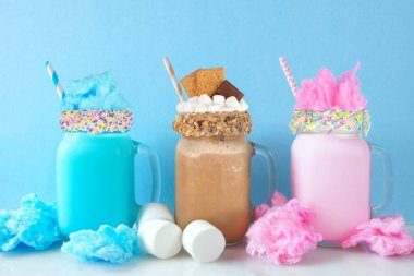 Mason kavanozundaki renkli milkshake 'ler pastel mavi arka planda. Mavi ve pembe pamuk şeker ve çikolatalı tatlı içecekler..