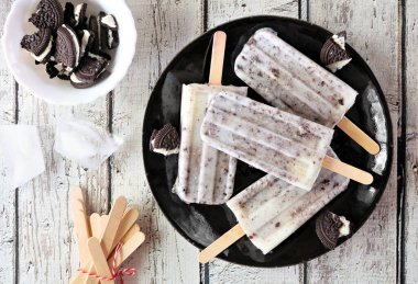 Kurabiyeler ve kremalı dondurmalar siyah bir tabakta. Beyaz ahşap zemin üzerinde üst görünüm.