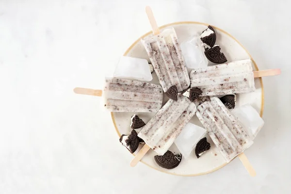 Cookies and cream ice pops on a plate. Overhead view on a white marble background.