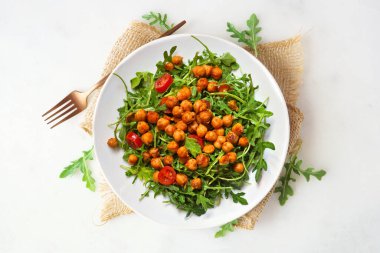 Roka salatası ve baharatlı nohut. Beyaz mermer bir arka plan üzerinde ahşap bir plaka üzerinde yukarıdan görünüm.