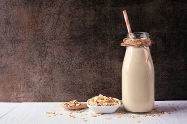 Antika bir şişede yulaf sütü ve malzemeler. Vejetaryen, bitki bazlı, sütsüz. Koyu bir arkaplan karşısında yan görünüm.