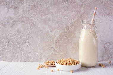 Şişe içinde soya sütü ve malzemeler. Vejetaryen, bitki bazlı, sütsüz. Parlak bir arkaplan karşısında yan görünüm.