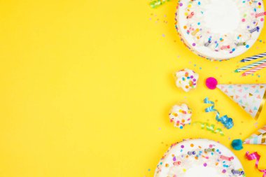 Birthday party side border on a yellow background. Top view with cakes, party hats and confetti. Copy space.