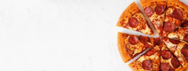 Pepperoni pizza close up with cut slices. Above view over a white marble banner background. Copy space.